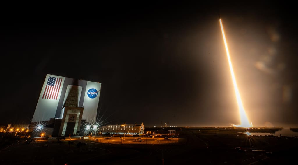 Un lanzamiento nocturno junto al reloj de cuenta regresiva y la bandera de la NASA en Kennedy Space Center
