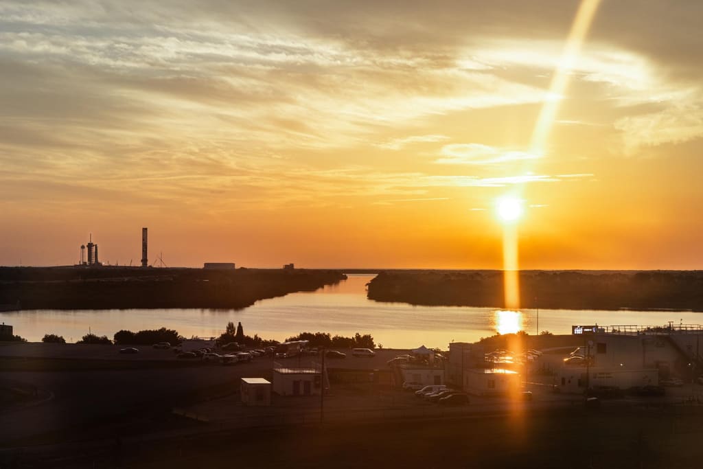 Un cohete despegando al amanecer, su estela brillando sobre el agua